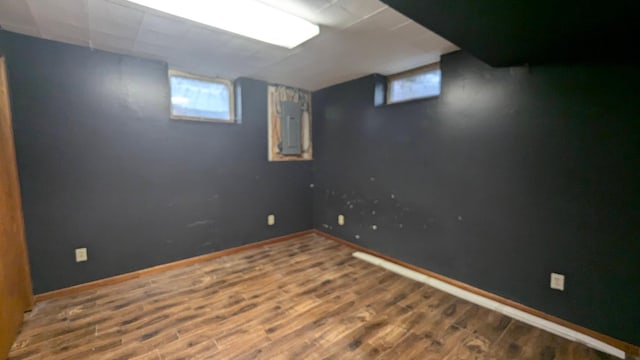 below grade area with electric panel, baseboards, and wood finished floors