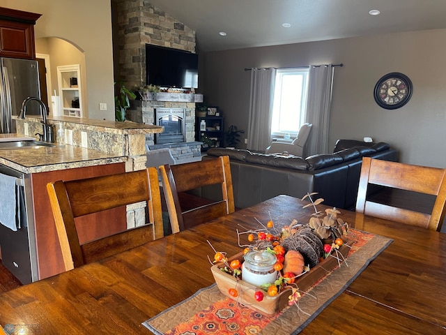 dining space with dark hardwood / wood-style flooring, a stone fireplace, vaulted ceiling, and sink