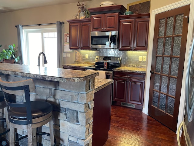 kitchen featuring a breakfast bar, dark wood-type flooring, sink, decorative backsplash, and appliances with stainless steel finishes