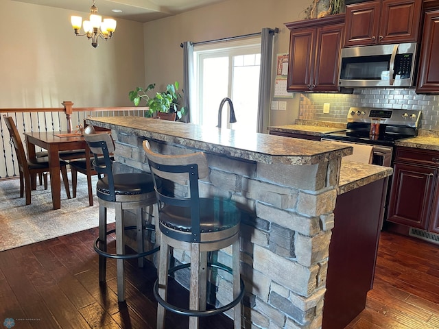 kitchen featuring pendant lighting, dark wood-type flooring, an inviting chandelier, decorative backsplash, and stainless steel appliances