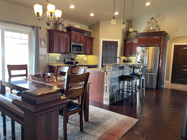 kitchen featuring stainless steel appliances, a notable chandelier, decorative light fixtures, decorative backsplash, and a center island with sink