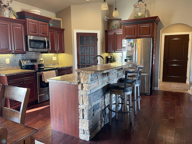 kitchen featuring decorative backsplash, stainless steel appliances, decorative light fixtures, dark hardwood / wood-style floors, and an island with sink