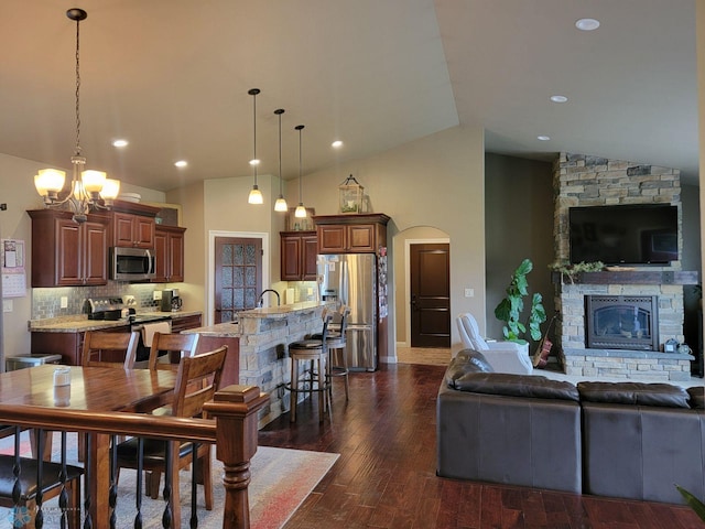 dining room with high vaulted ceiling, sink, dark hardwood / wood-style floors, a fireplace, and a notable chandelier