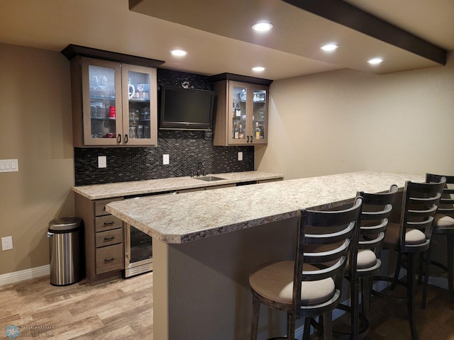 bar featuring dark brown cabinetry, sink, light stone counters, light hardwood / wood-style flooring, and backsplash