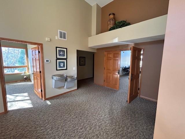 hallway featuring high vaulted ceiling and dark colored carpet