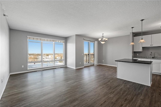 unfurnished living room featuring a chandelier, a textured ceiling, dark hardwood / wood-style floors, and sink