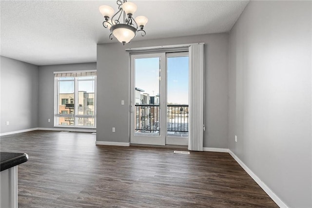 unfurnished room with a chandelier, a textured ceiling, and dark wood-type flooring