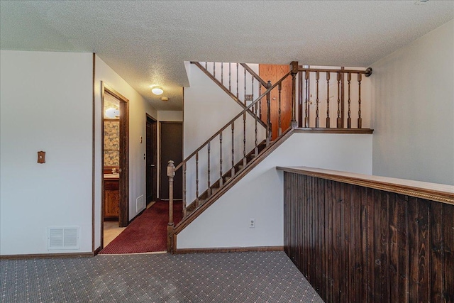 staircase featuring a textured ceiling and carpet floors