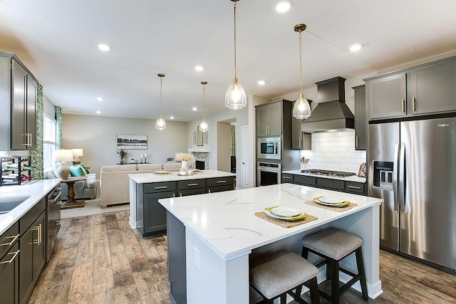 kitchen with pendant lighting, appliances with stainless steel finishes, a kitchen island, dark wood-type flooring, and premium range hood