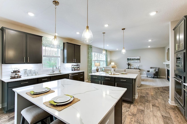 kitchen with decorative light fixtures, a center island, sink, stainless steel appliances, and light stone counters