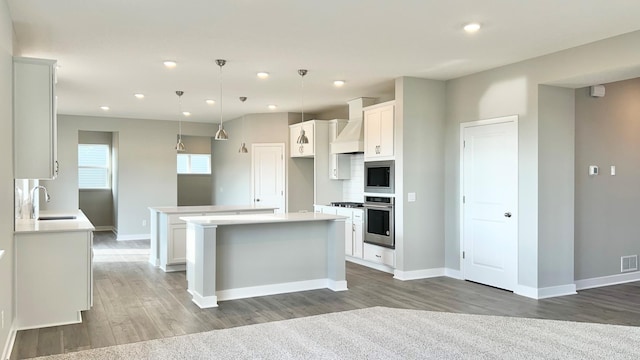 kitchen featuring white cabinetry, custom exhaust hood, appliances with stainless steel finishes, decorative light fixtures, and a center island