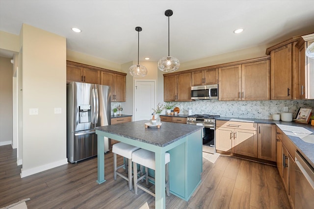 kitchen with tasteful backsplash, hanging light fixtures, dark hardwood / wood-style flooring, appliances with stainless steel finishes, and a center island