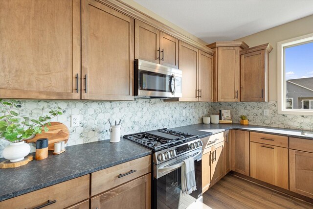 kitchen with appliances with stainless steel finishes, dark stone countertops, hardwood / wood-style flooring, and backsplash