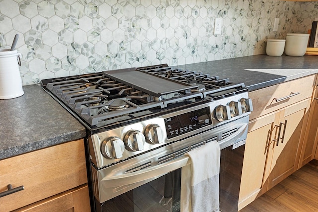 kitchen with dark stone countertops, hardwood / wood-style flooring, stainless steel stove, and tasteful backsplash