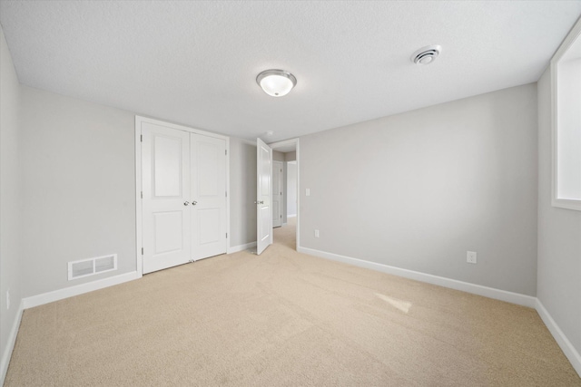 unfurnished bedroom with a closet, light carpet, and a textured ceiling