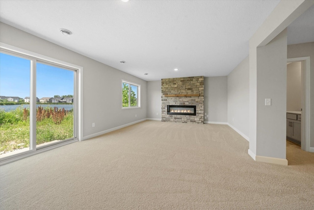 unfurnished living room featuring a water view, a fireplace, and light colored carpet