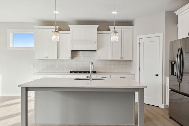 kitchen with decorative light fixtures, a kitchen island with sink, and stainless steel fridge