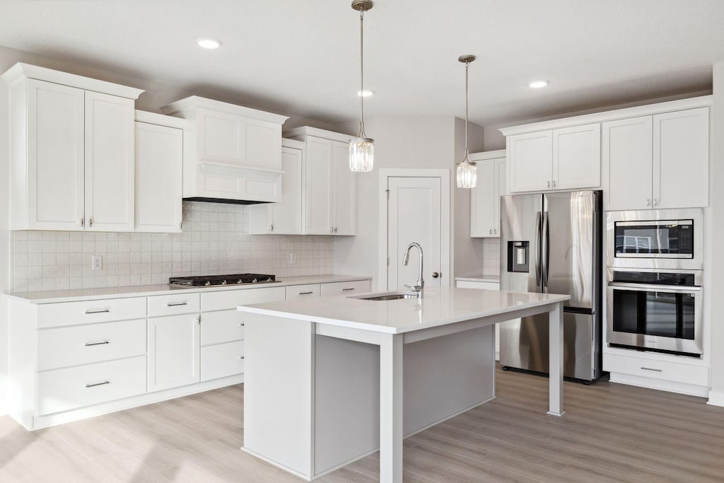 kitchen with sink, white cabinetry, an island with sink, hanging light fixtures, and appliances with stainless steel finishes