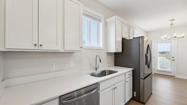 kitchen featuring a notable chandelier, sink, hanging light fixtures, appliances with stainless steel finishes, and white cabinets