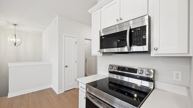 kitchen with white cabinetry, stainless steel appliances, hanging light fixtures, a chandelier, and light hardwood / wood-style flooring