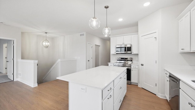 kitchen with white cabinets, appliances with stainless steel finishes, pendant lighting, and a center island