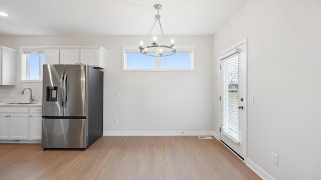 kitchen featuring white cabinetry, sink, hanging light fixtures, stainless steel fridge, and a chandelier