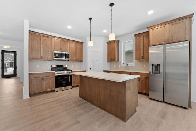 kitchen with a kitchen island, appliances with stainless steel finishes, decorative light fixtures, sink, and light hardwood / wood-style floors