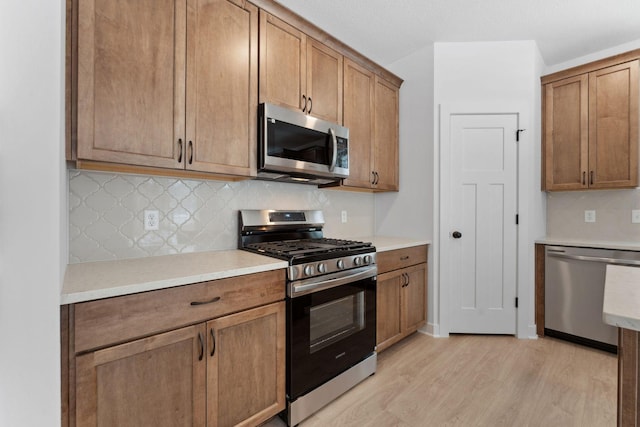 kitchen with appliances with stainless steel finishes, backsplash, and light hardwood / wood-style floors