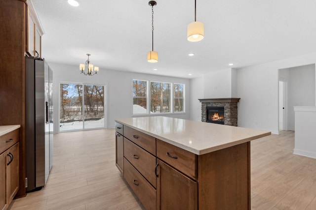 kitchen featuring hanging light fixtures, stainless steel fridge, a fireplace, and light hardwood / wood-style flooring