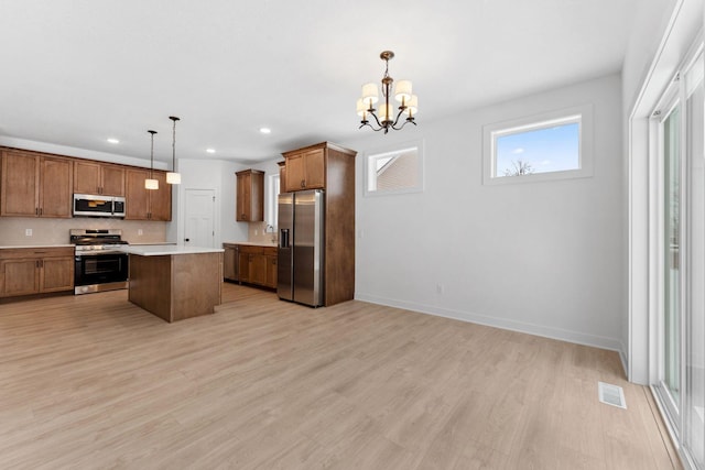 kitchen with a kitchen island, appliances with stainless steel finishes, light hardwood / wood-style flooring, and decorative light fixtures