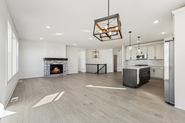 kitchen featuring decorative backsplash, a kitchen island, light wood-type flooring, stainless steel appliances, and decorative light fixtures