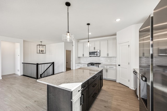 kitchen with appliances with stainless steel finishes, light hardwood / wood-style flooring, white cabinetry, and hanging light fixtures