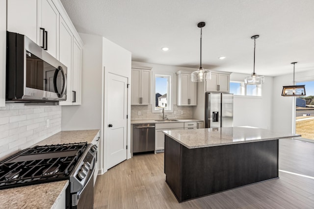 kitchen featuring appliances with stainless steel finishes, sink, a center island, hanging light fixtures, and light hardwood / wood-style floors