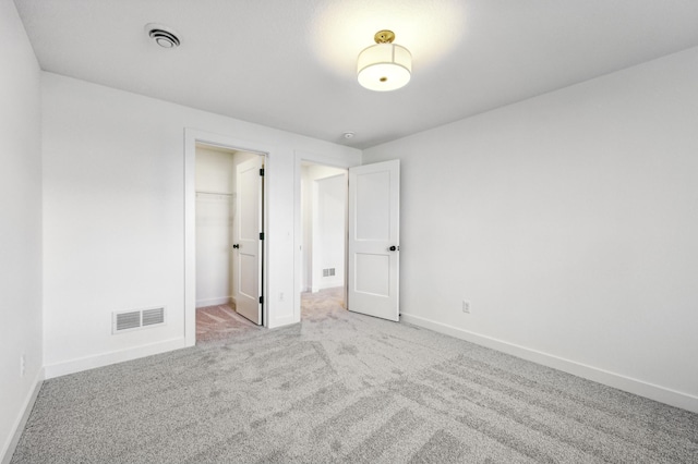 unfurnished bedroom with a closet, a walk in closet, and light colored carpet