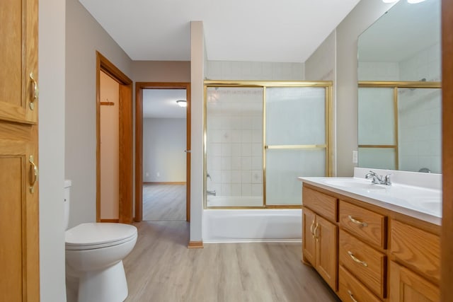 full bathroom with toilet, combined bath / shower with glass door, hardwood / wood-style floors, and vanity