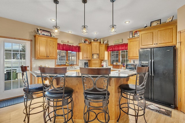 kitchen featuring light wood-type flooring, tasteful backsplash, black refrigerator with ice dispenser, decorative light fixtures, and a center island