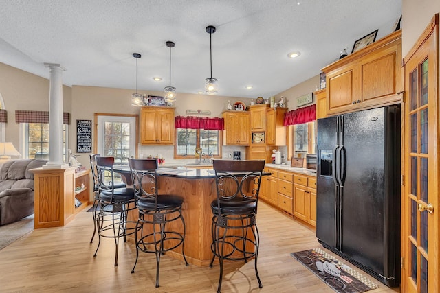 kitchen featuring a kitchen island, black fridge with ice dispenser, light hardwood / wood-style flooring, and decorative columns