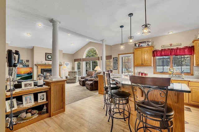 kitchen featuring a kitchen bar, light wood-type flooring, backsplash, and decorative columns