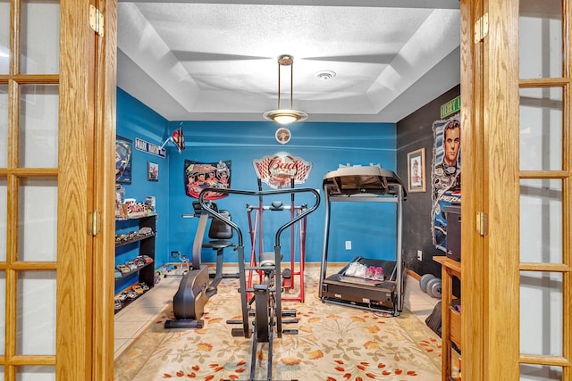 workout room with a tray ceiling, tile patterned flooring, and a textured ceiling