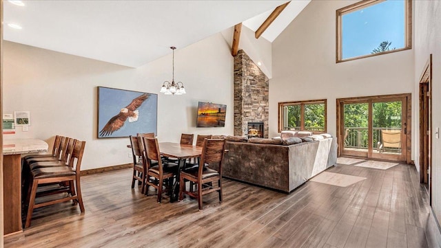 dining space with baseboards, wood finished floors, a stone fireplace, high vaulted ceiling, and a notable chandelier