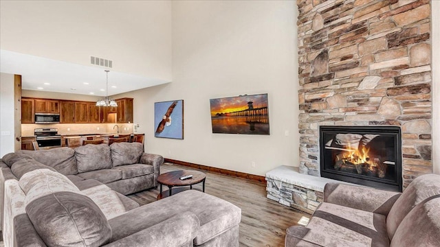 living area with baseboards, visible vents, a towering ceiling, wood finished floors, and a stone fireplace