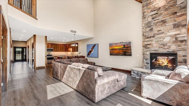 living area with baseboards, visible vents, dark wood-style floors, a high ceiling, and a fireplace