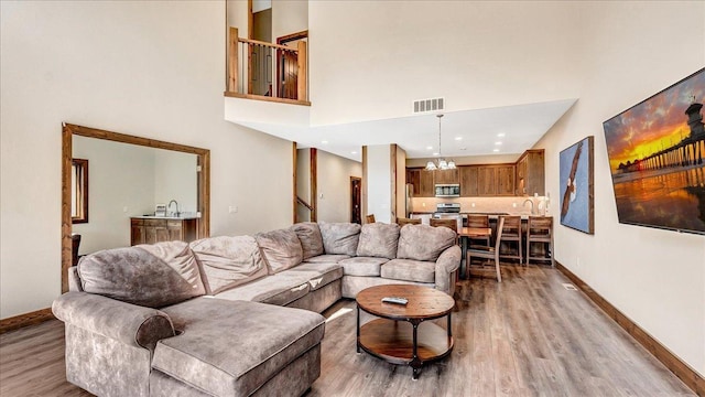 living room with a high ceiling, wood finished floors, visible vents, baseboards, and an inviting chandelier