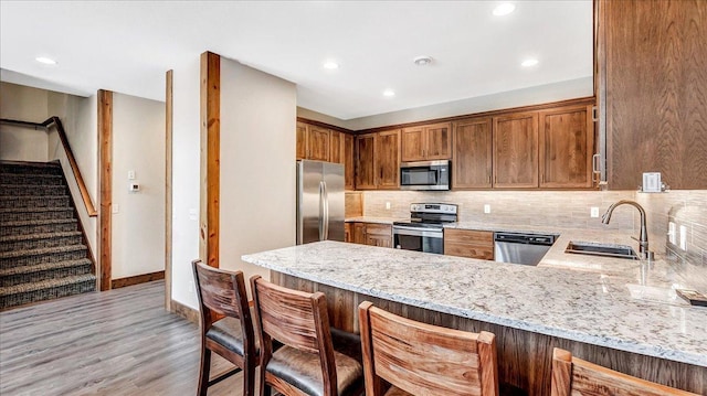 kitchen with light stone counters, a peninsula, a sink, appliances with stainless steel finishes, and tasteful backsplash