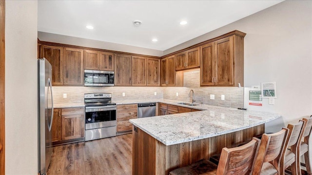 kitchen featuring tasteful backsplash, appliances with stainless steel finishes, a peninsula, light wood-style floors, and a sink