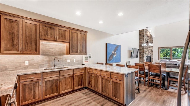 kitchen with brown cabinets, a peninsula, a sink, light wood-type flooring, and backsplash