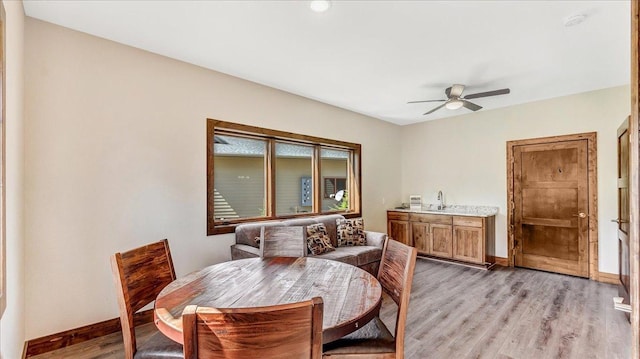 dining area featuring a ceiling fan, light wood-style flooring, and baseboards