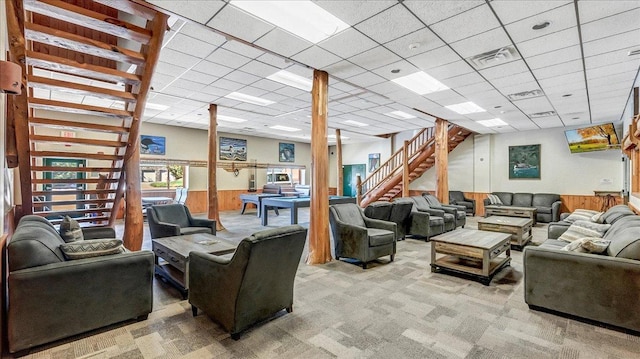 living area featuring wooden walls, visible vents, light colored carpet, a wainscoted wall, and stairs