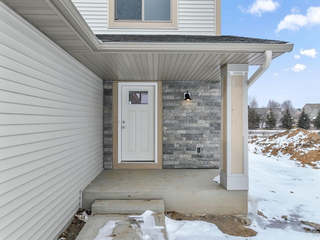 snow covered property entrance featuring stone siding