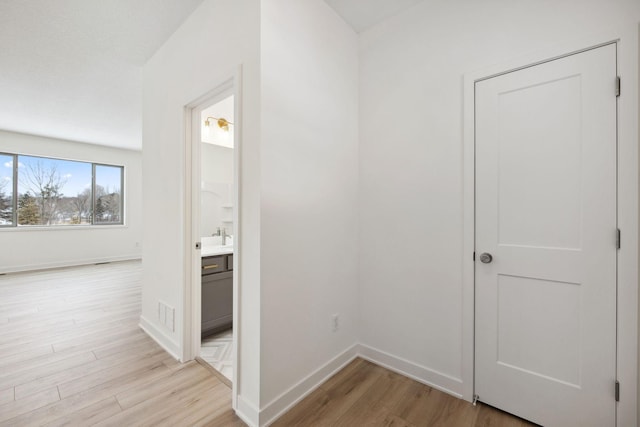 hall featuring light wood-style flooring, visible vents, and baseboards